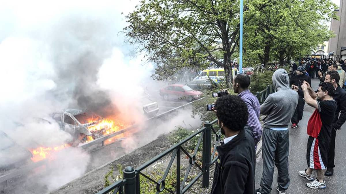 Ohikulkijat katsoivat mellakoitsijoiden sytyttämien autojen paloa Tukholman Rinkebyssä toukokuussa 2013.