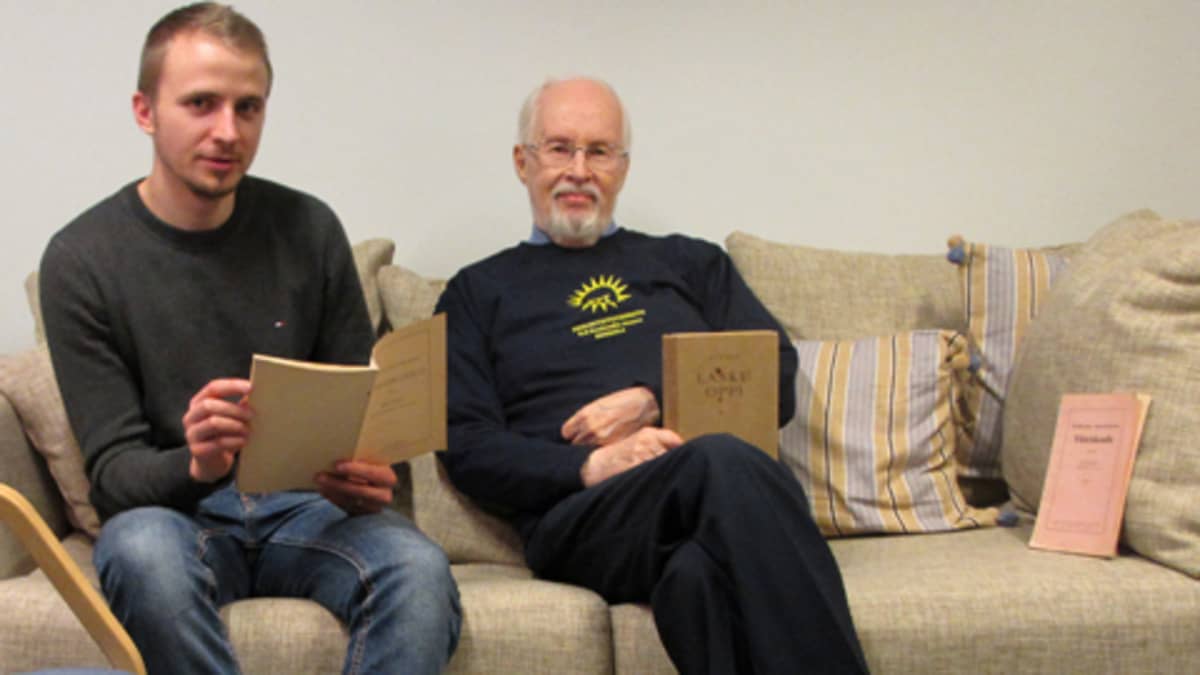 Kuvassa kaksi miestä istuu sohvalla vanhojen kirjojen kanssa