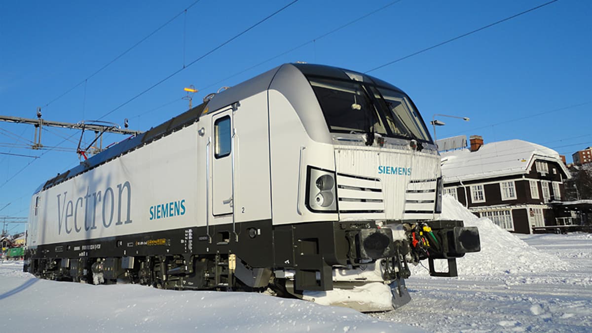 Valkoinen Siemens Vectron -veturi lumisessa maisemassa.
