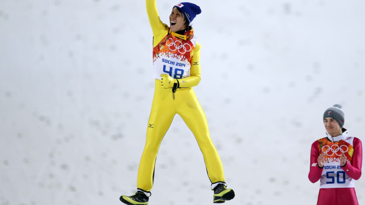 Japanin Noriaki Kasai hyppää ilmaan palkintoseremoniassa. Puolan Kamil Stoch antaa aplodit.