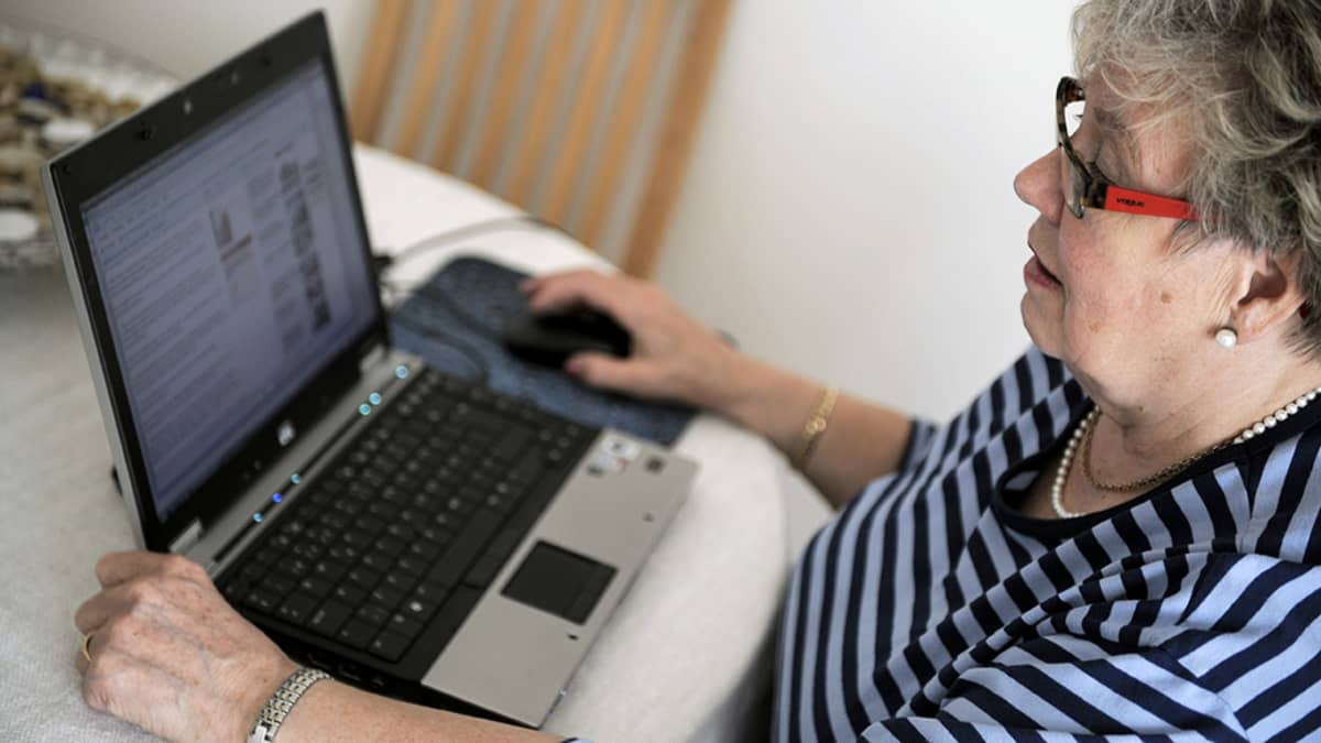 Iäkäs nainen käyttää tietokonetta kotonaan.