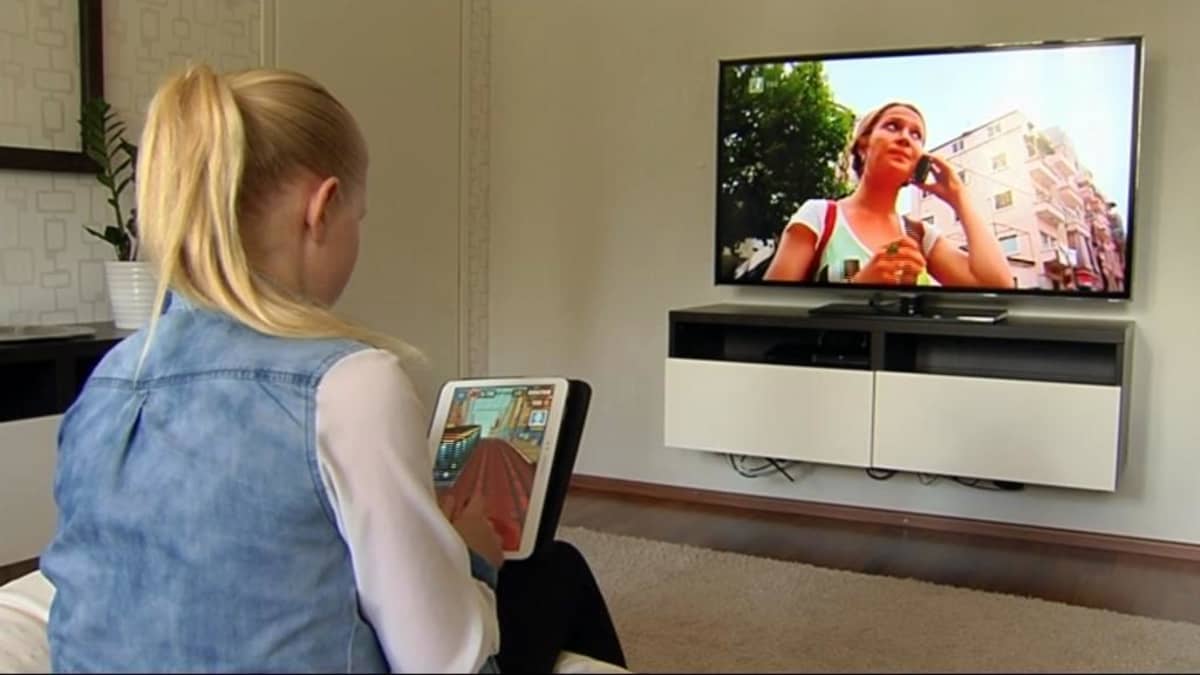 Tyttö käyttää tablet-tietokonetta tv:n ääressä