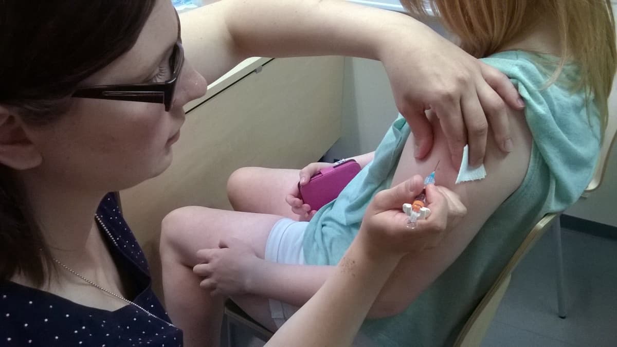 Terveydenhoitaja laittaa tytölle rokotteen käsivarteen