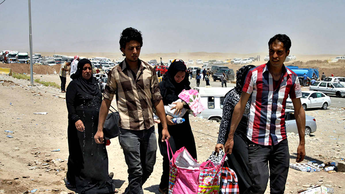 Irakilaiset siivilit ovat paenneet levottomuuksia Mosulista kohti Erbiliä. Kaksi nuorta miestä kantaa vaaleanpunaista muovikassia, takanaan kolme mustaan pukeutunutta naista.