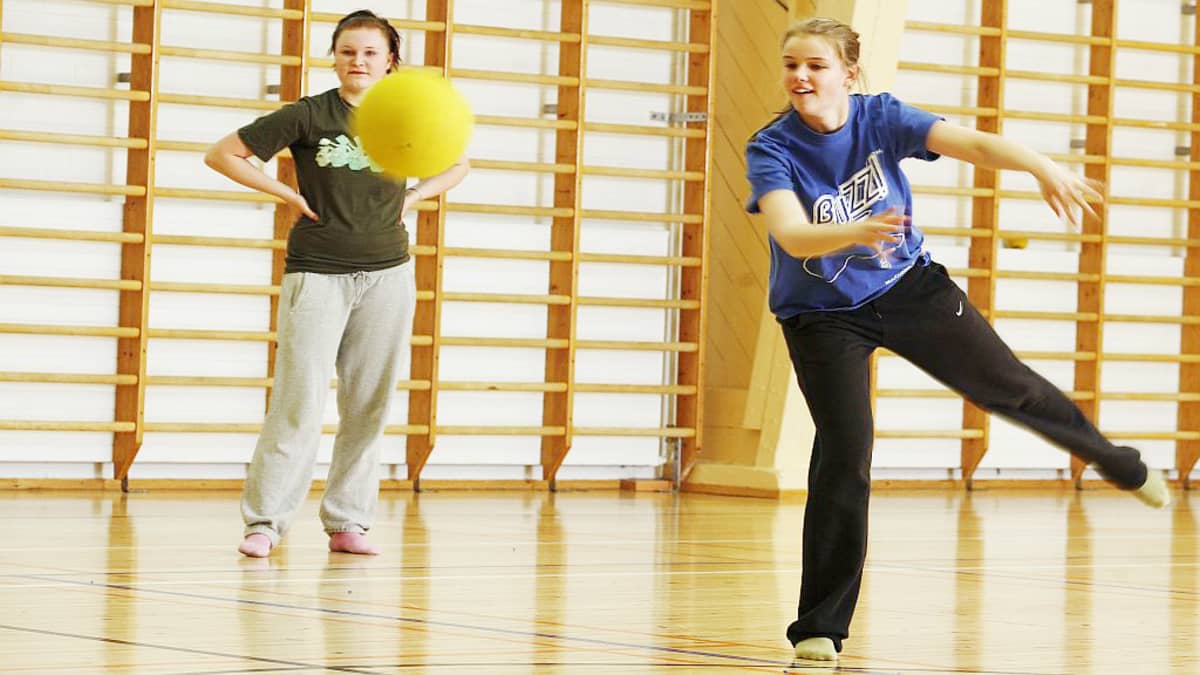 Kaksi tyttöä pelaa palloa liikuntasalissa.