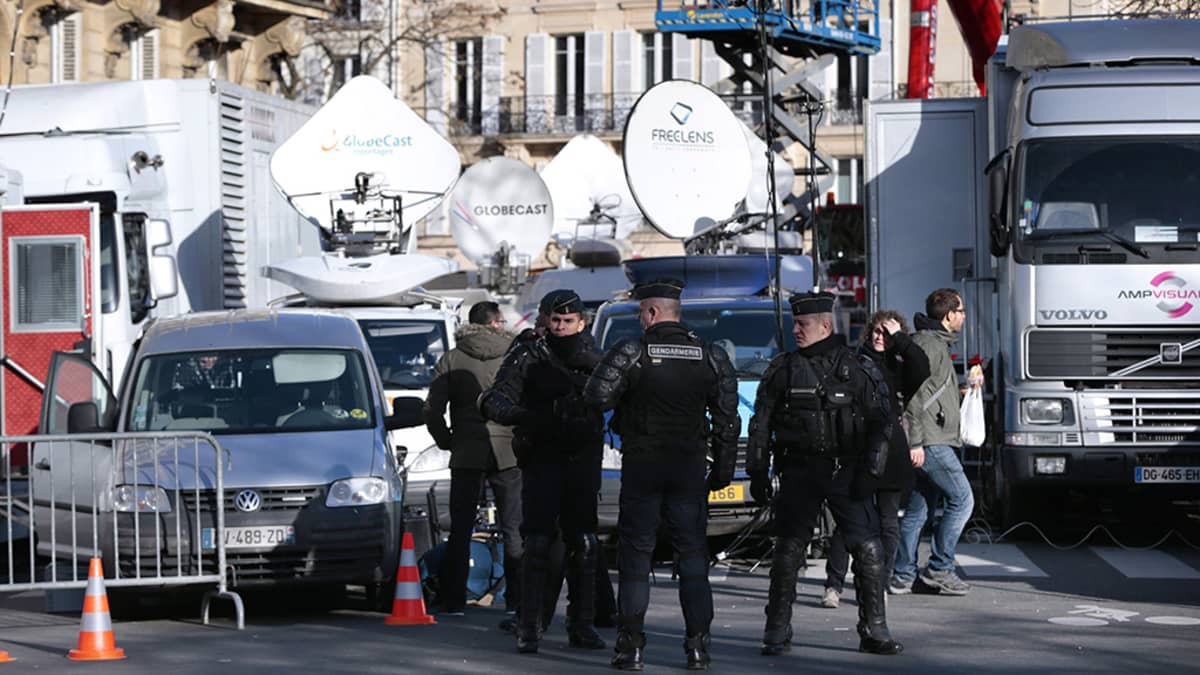Poliisit vartioivat median lähetysautoja kun ihmiset kokoontuivat Place de la Republiquelle Pariisissa sunnuntaina.