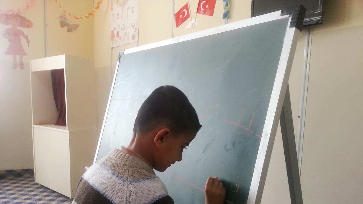 Syyrialaispoika harjoittelee kirjoittamista äidinkielen tunnilla yhdessä leirin kolmesta koulusta.