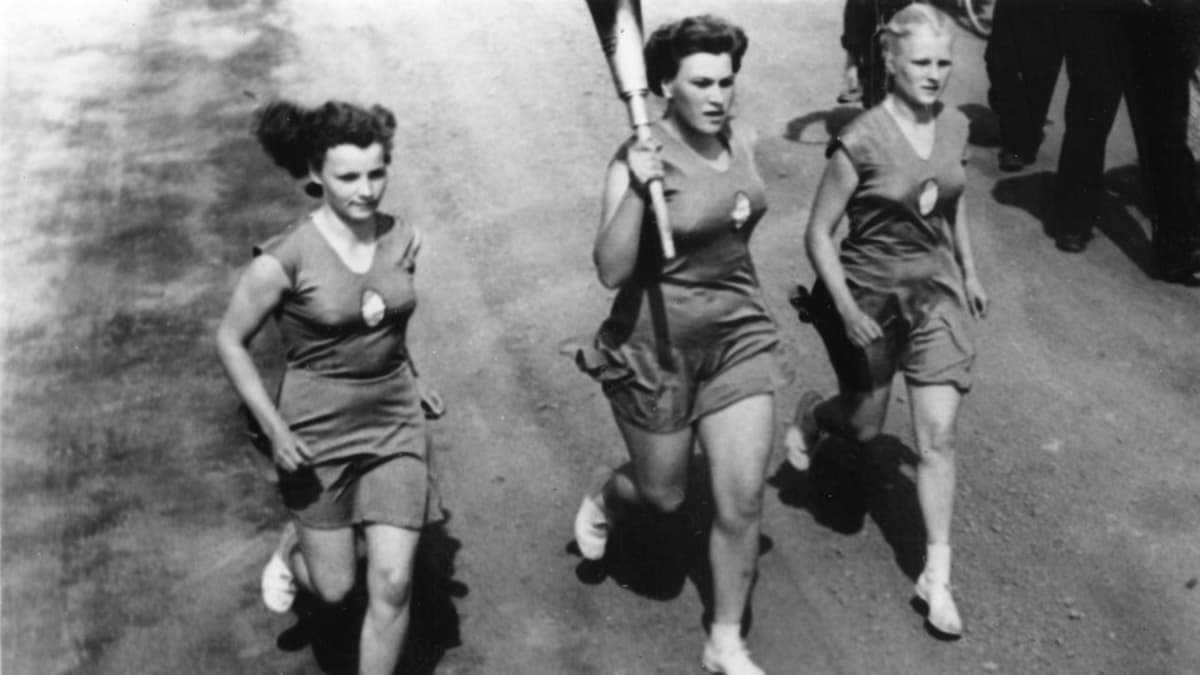 Soihtuviesti Saloisissa 11.7.1952. Soihdunkantaja ja kaksi saattajaa juoksevat maantiellä.