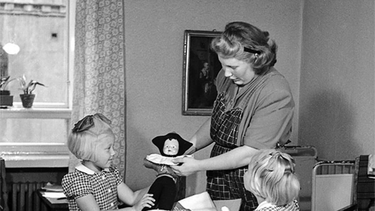 Äiti lapsineen katselemassa äitiyspakkauksen sisältöä 1950-luvulla.