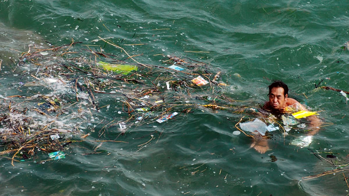 Kiinalainen mies ui meressä kelluvien roskien keskellä Qingdaossa.