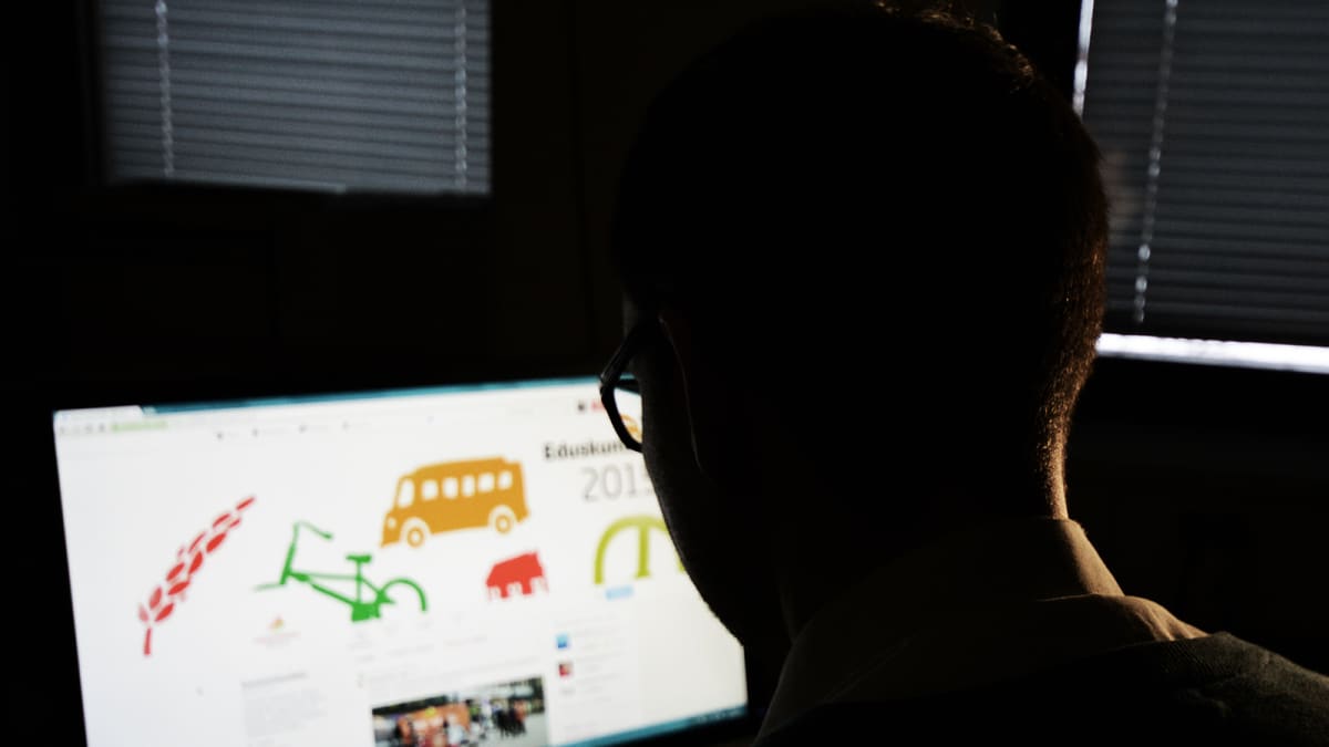Mies istuu pimeässä huoneessa tietokoneella.