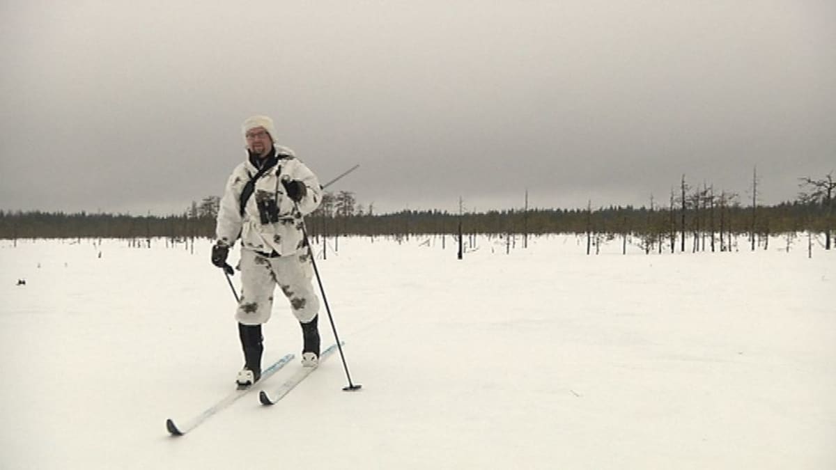 Mies hiihtää lumipuvussa avosuolla