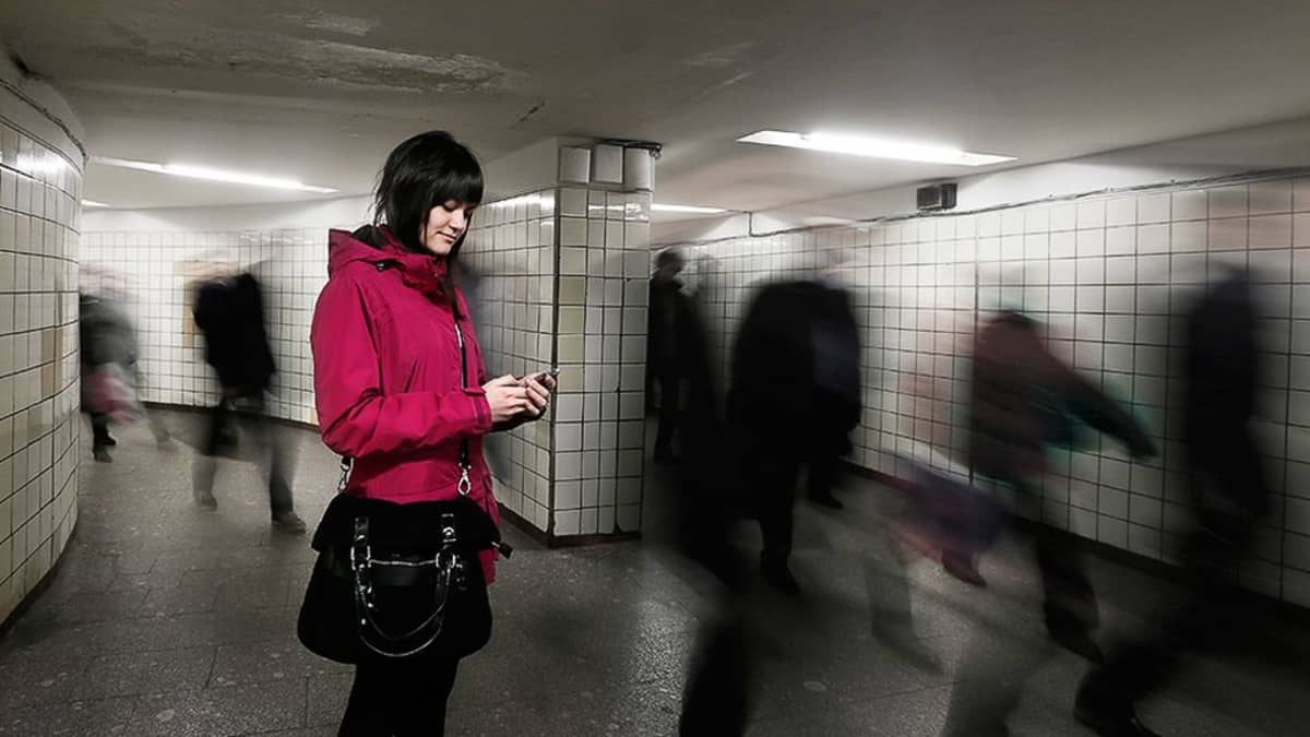Nuori nainen käyttää kännykkää metroasemalla.