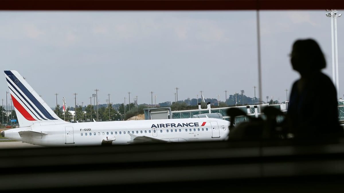 Nainen katselee tummennetun ikkunan läpi Charles de Gaullen lentokentälle. Edessä näkyy Air Francen lentokone, matkustaja on siluetissa.