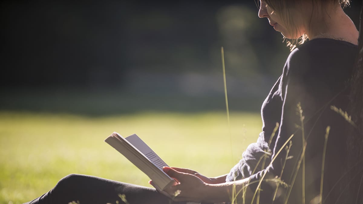 Nainen lukee kirjaa luonnossa.