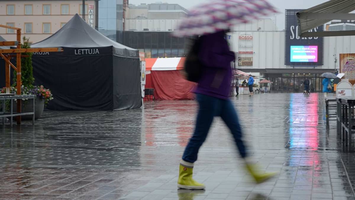 Ihminen kävelee sateenvarjon kanssa, taustalla Kuopion tori