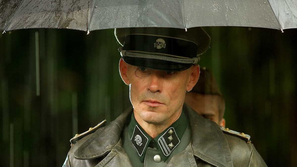 Mies seisoon natsiupseerin asusssa sateenvarjon alla sateessa