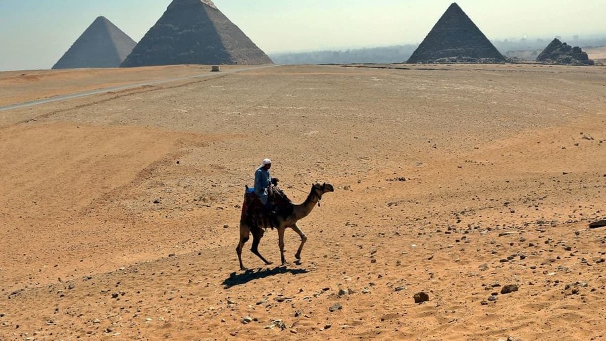 Turistiopas ratsastaa kamelilla Gizan pyramidien edustalla.