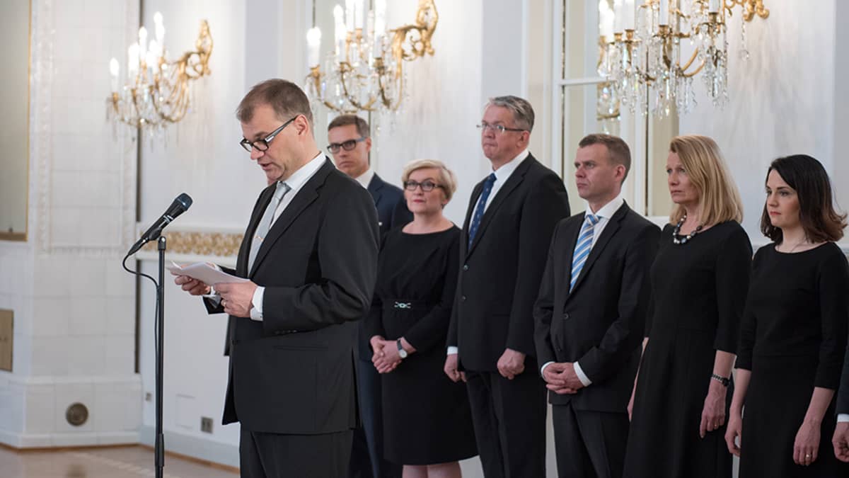 Juha Sipilä puhuu ja takana seisoo hallitus
