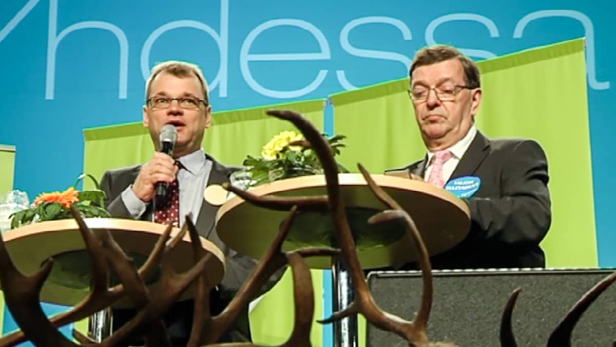 Juha Sipilä ja Paavo Väyrynen esiintymislavalla pöytien ääressä. Juha Sipilä valittiin keskustan puheenjohtajaksi vuonna 2012. Puolueen kunniapuheenjohtaja Paavo Väyrynen ei päässyt vaalien toiselle kierrokselle.