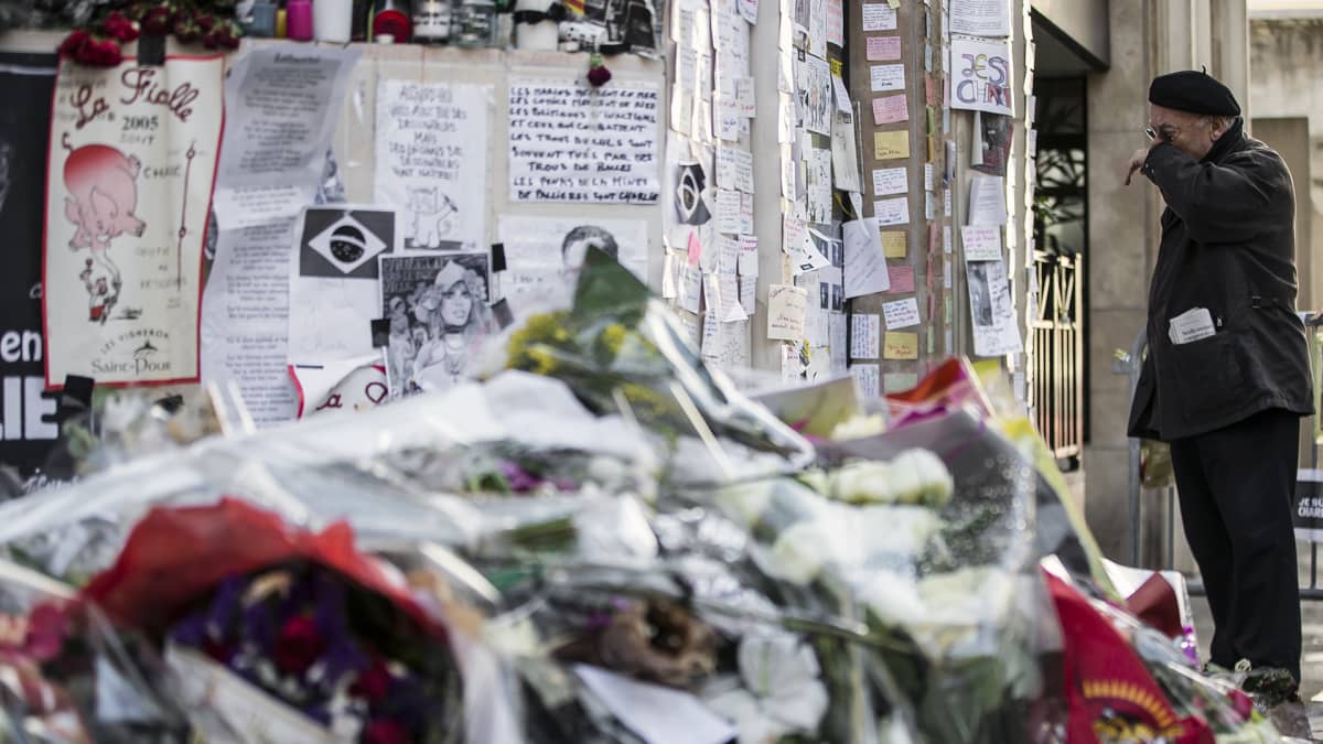 Mies kunnioittaa terrori-iskussa kuolleiden muistoa satiirilehti Charlie Hebdon toimituksen lähellä Pariisissa.