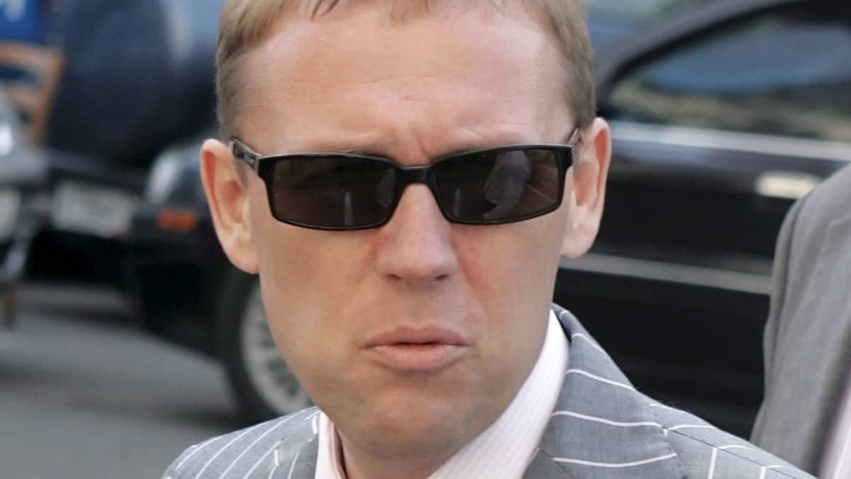Andrei Lugovoi mustat lasit pääsään, raidallisessa harmaassa puvussa, vaaleanpunainen kravatti kaulassaan.