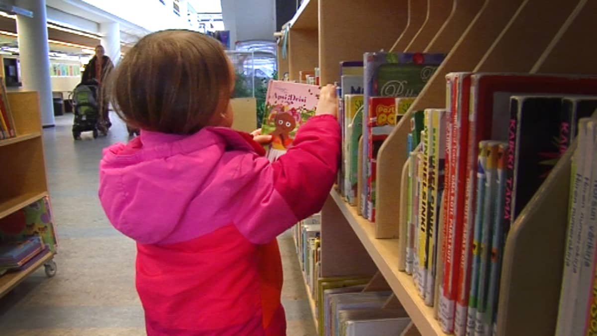 Lapsi etsii kirjaston hyllystä luettavaa.