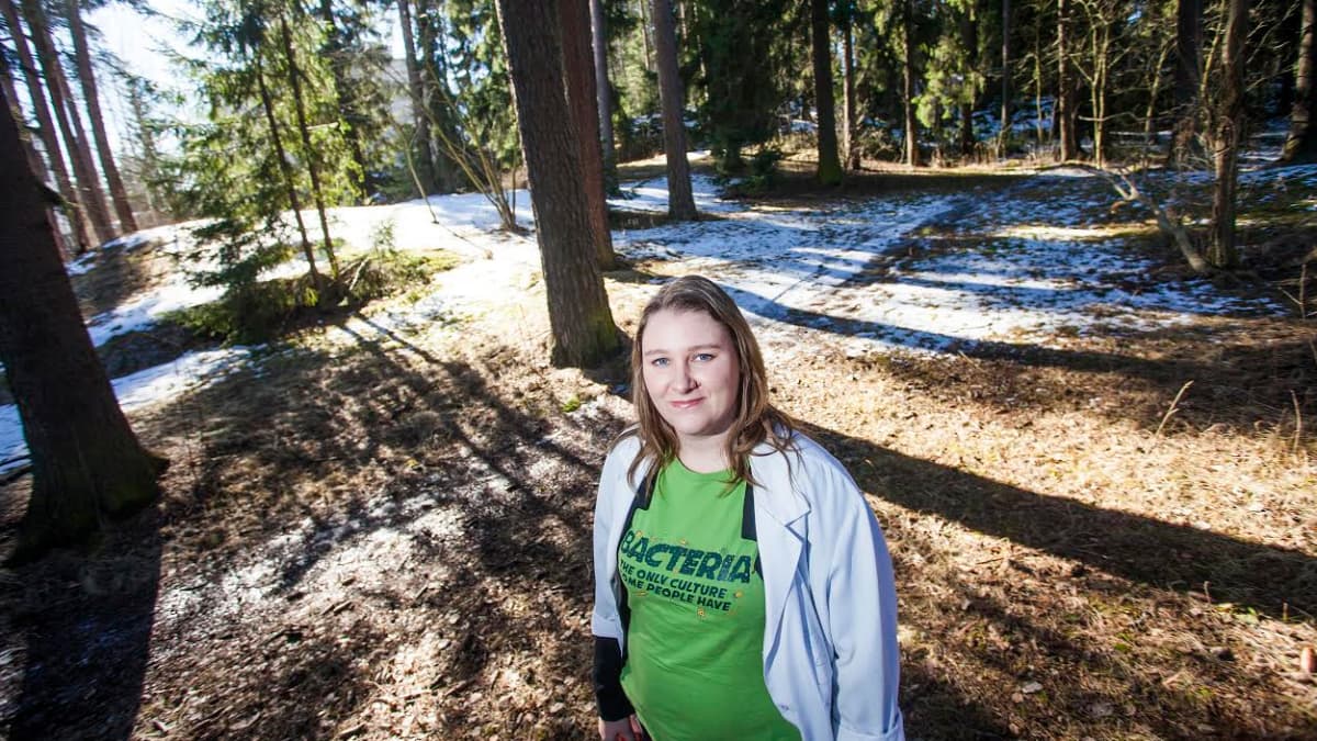 Alzheimertutkija Eloise Mikkonen seisoo puiden keskellä metsässä.
