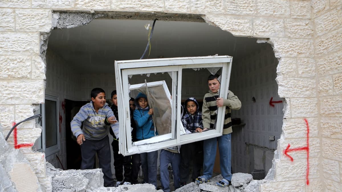 Kuusi pikkupoikaa pitelee paikaltaan irrotettua ikkunaa talon raunioissa. 