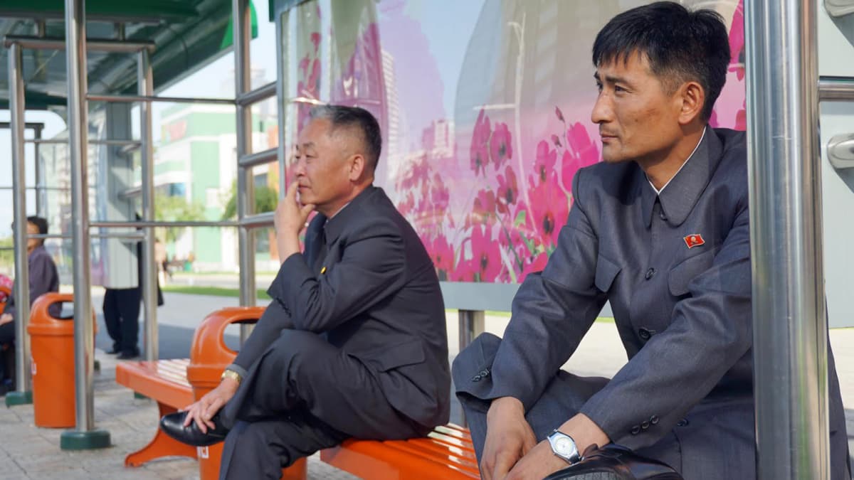 Miehet istuvat upouudella bussipysäkillä ”Tulevaisuuden tiedemiesten kadun” pilvenpiirtäjäalueella.