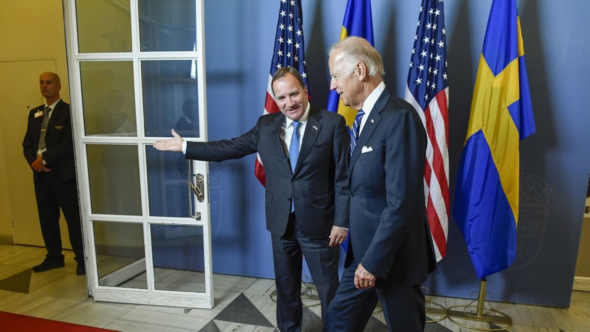 Stefan Löfven ohjaa kädellään Joe Bidenia kohti ovea. Biden ottaa askelta kohti ovea. Molemmilla on tummansiniset puvut ja erilaiset siniset kravatit. Miehet hymyilevät. Seinällä taustalla on Yhdysvaltain ja Ruotsin lippuja. Oven takana seisoo turvamies mustassa puvussa.