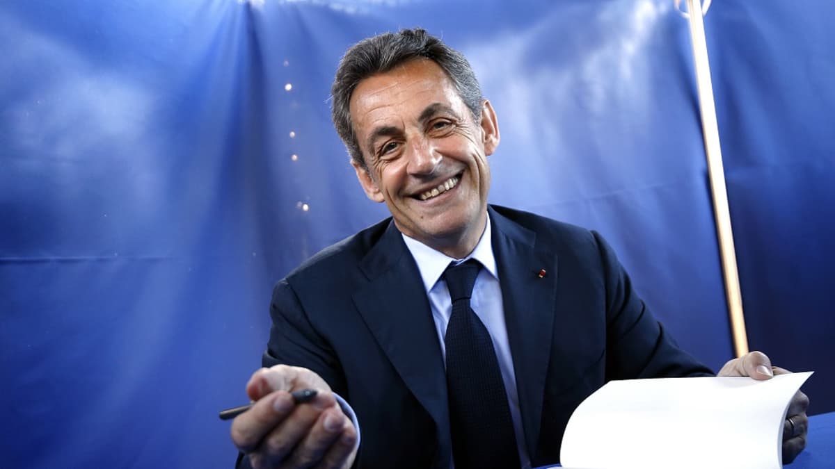 Nicolas Sarkozy katsoo kameraan ja virnistää.