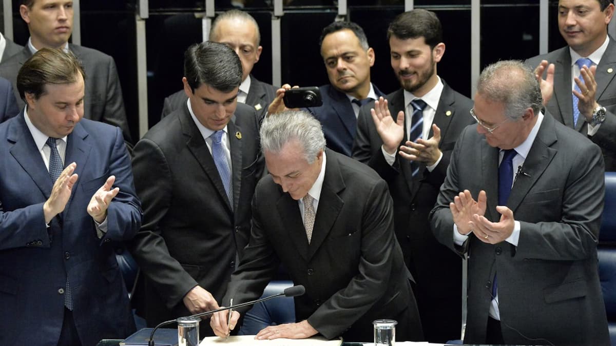 Joukko miehiä tummansävyisissä puvuissa seisoo Brasilian kongressissa. Temer kirjoittaa nimensä kirjaan. Muut taputtavat.