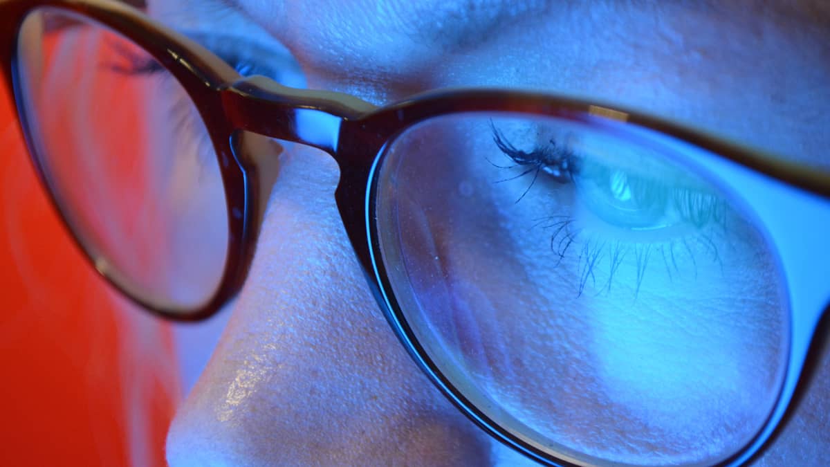 Naisen silmät, sininen valo heijastuu silmälaseista.