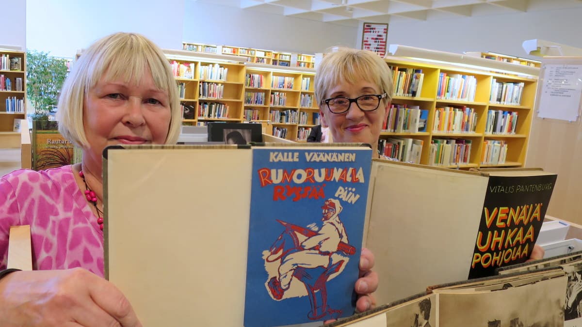 Kaksi naista pitävät kirjastossa käsissään vanhoja kirjoja
