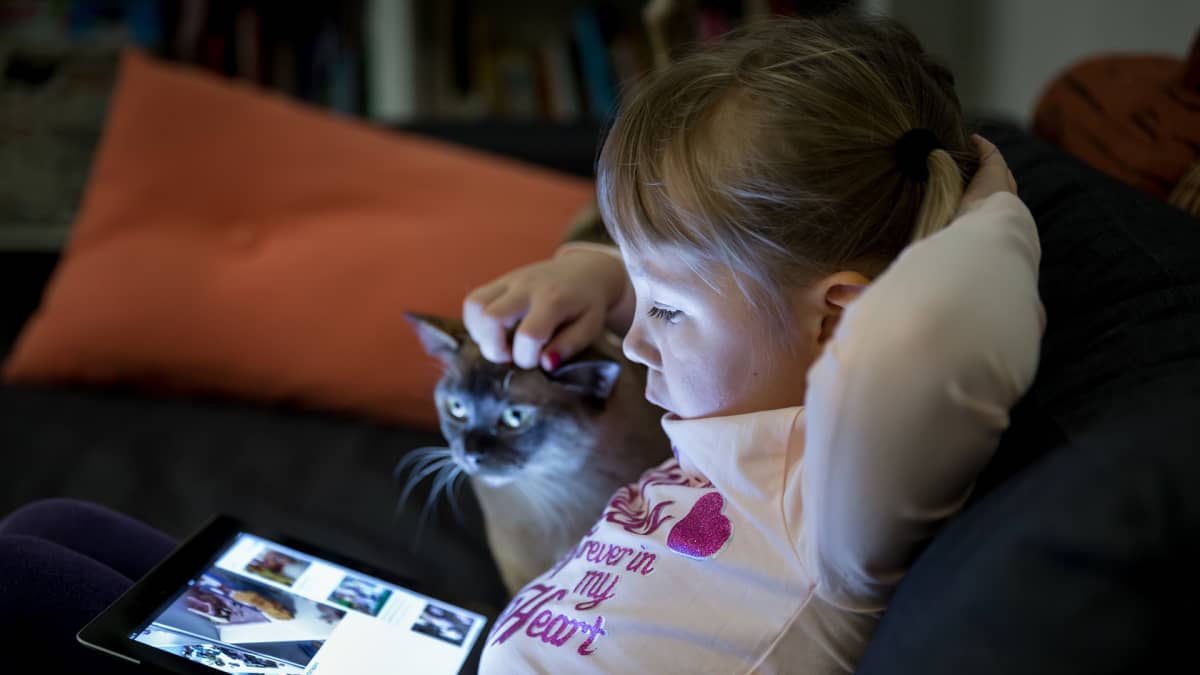 Viisivuotias Kaisla katselee iPadia, kuvassa myös perheen kissa.