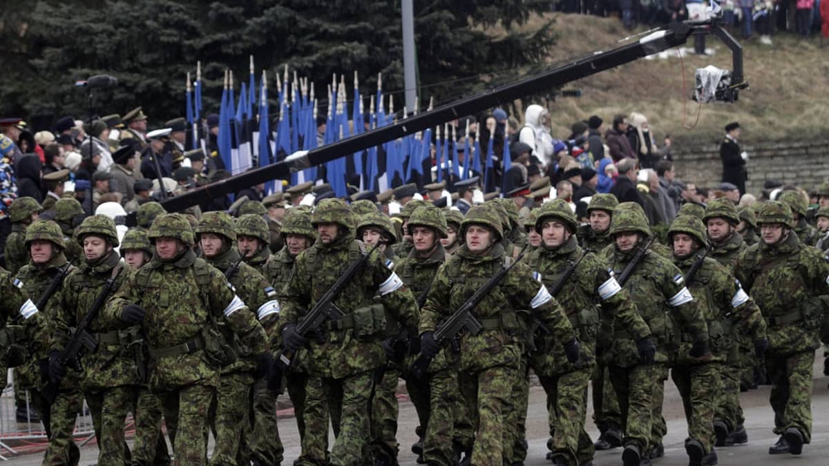 Vihreissä sotilasasuissa olevat sotilaat marssivat etualalla. Taustalla näkyy rivi Viron lippuja.