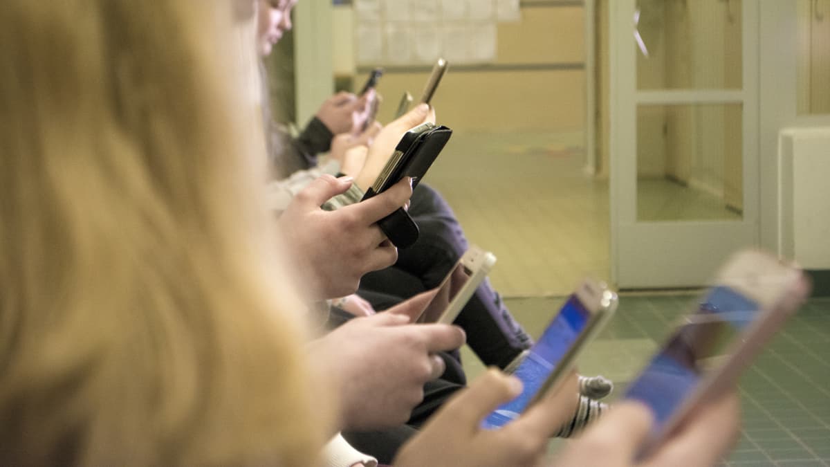 Lapset käyttävät kännyköitä koulun käytävällä.