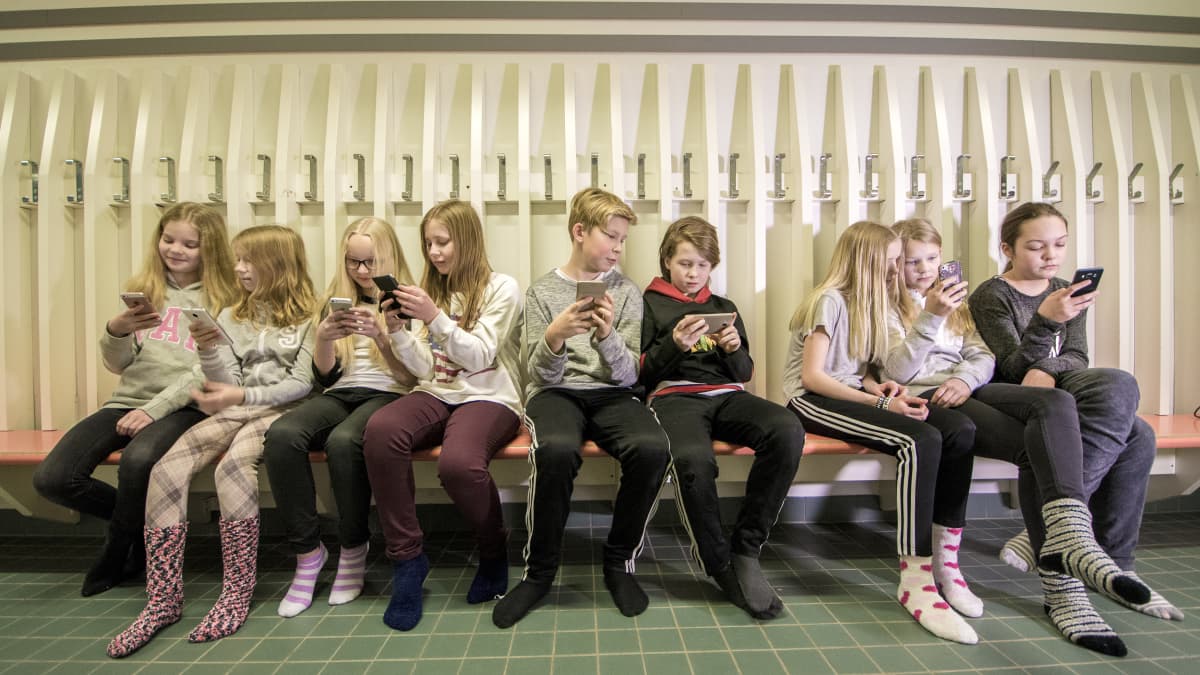 Lapset käyttävät kännyköitä koulun käytävällä.