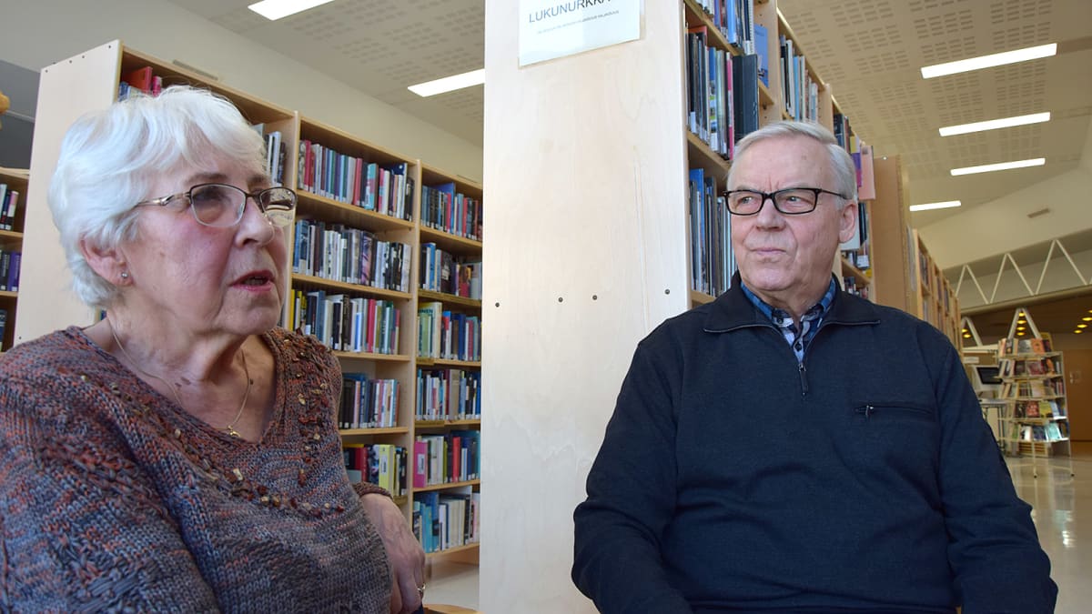 Nainen ja mies istuvat kirjastossa ja keskustelevat