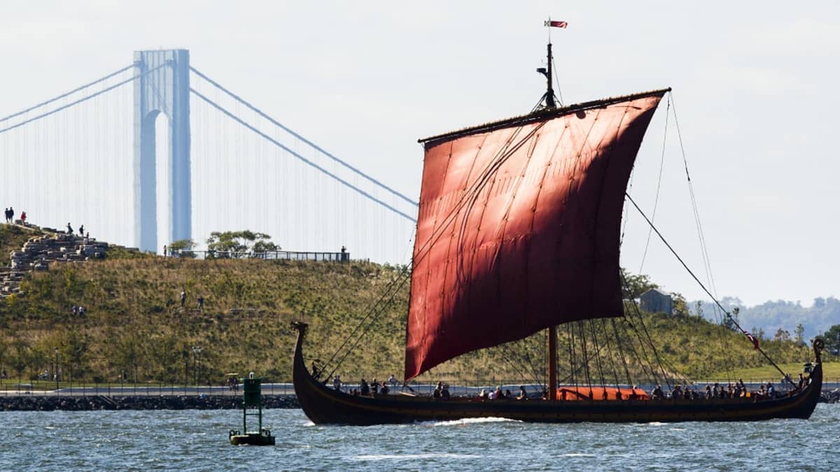 Iso punapurjeinen viikinkineve purjehtii sillan ohi. 