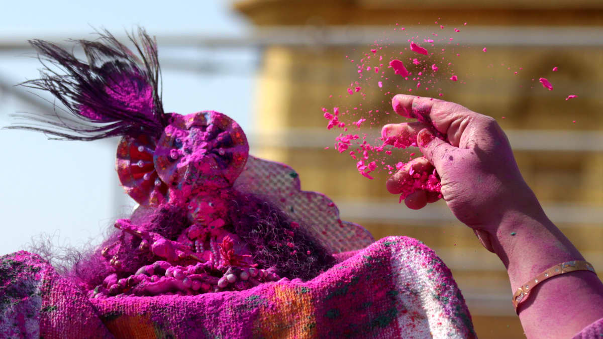 Nainen heittää punaista värijauhetta pienen Krishnan patsaan päälle Armitsarissa.