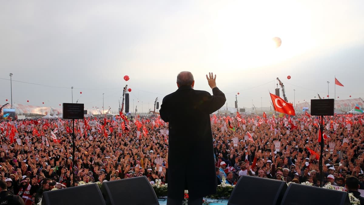 Presidentin selkä ja edessä valtava ihmisjoukko joilla Turkin lippuja.