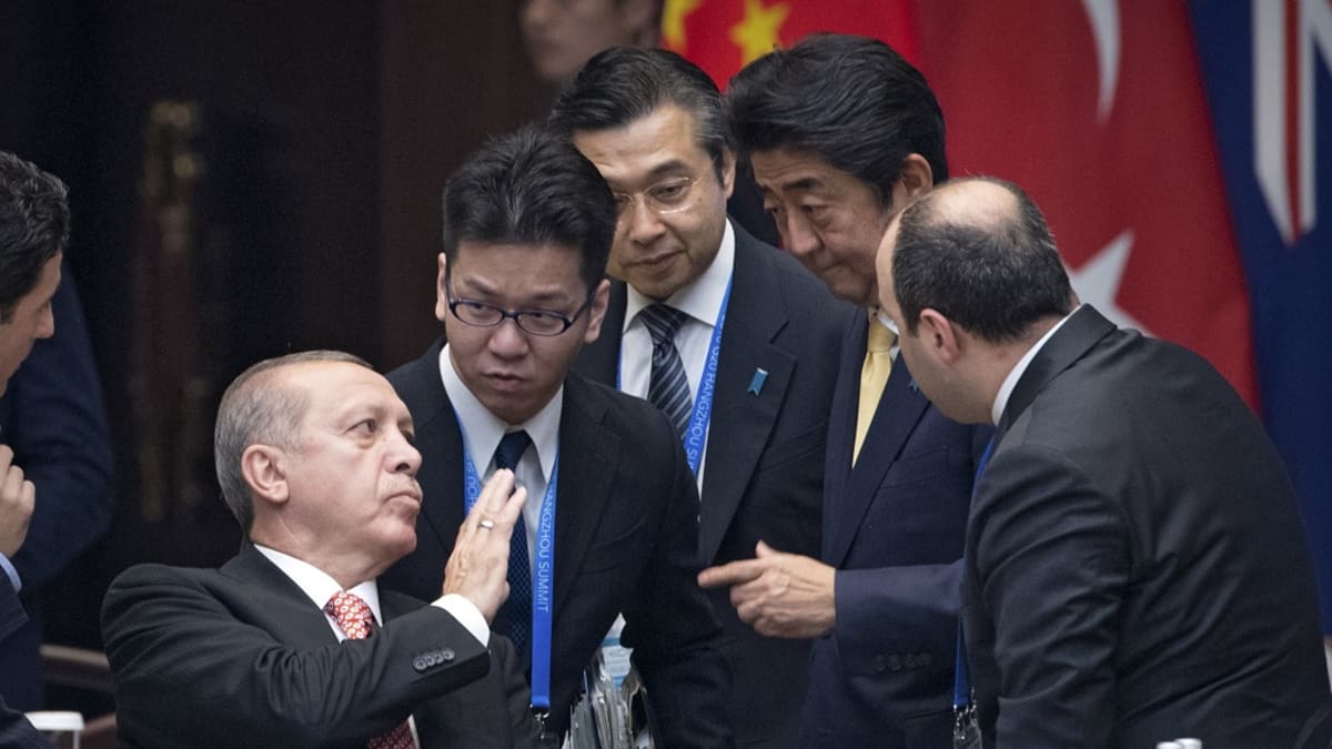 Erdoğan istuu, miehet ympärillä seisovat.