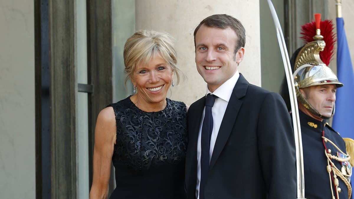 Brigitte Trogneux ja Emmanuel Macron vierekkäin palatsin ovella. Taustalla näkyy perinteisessä paraatiunivormussa oleva sotilas, joka pitää miekkaansa paljastettuna.