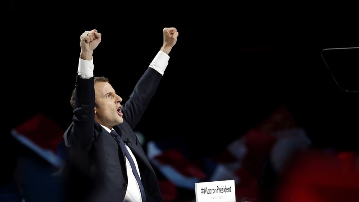 Tummaan pukuun pukeutunut Macron tuulettaa nyrkit ilmassa.