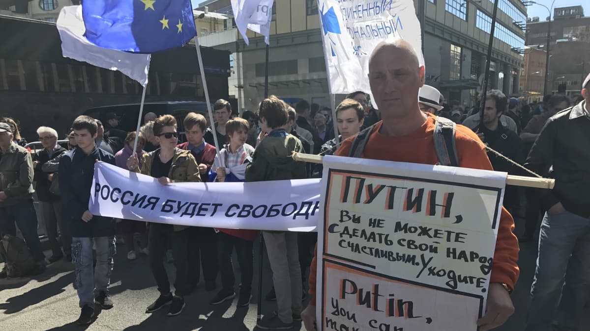 Mies, jolla Putinin eroa vaativa kyltti. Taustalla mielenosoittajia ja EU-lippu.