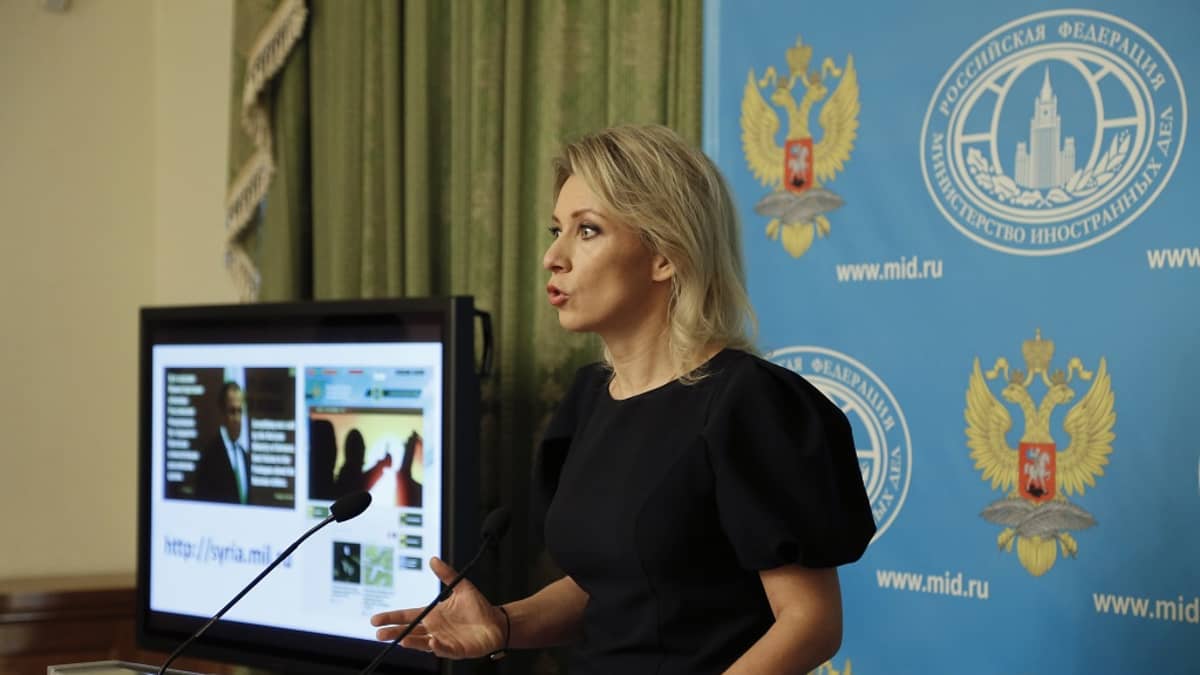 Musta-asuinen Zaharova puhuu puhujanpöntön takana. Taustalla näkyy Venäjän ulkoministeriön logoilla ja Venäjän vaakunakuvilla varusteltu sininen kangas ja vihreää verhoa.