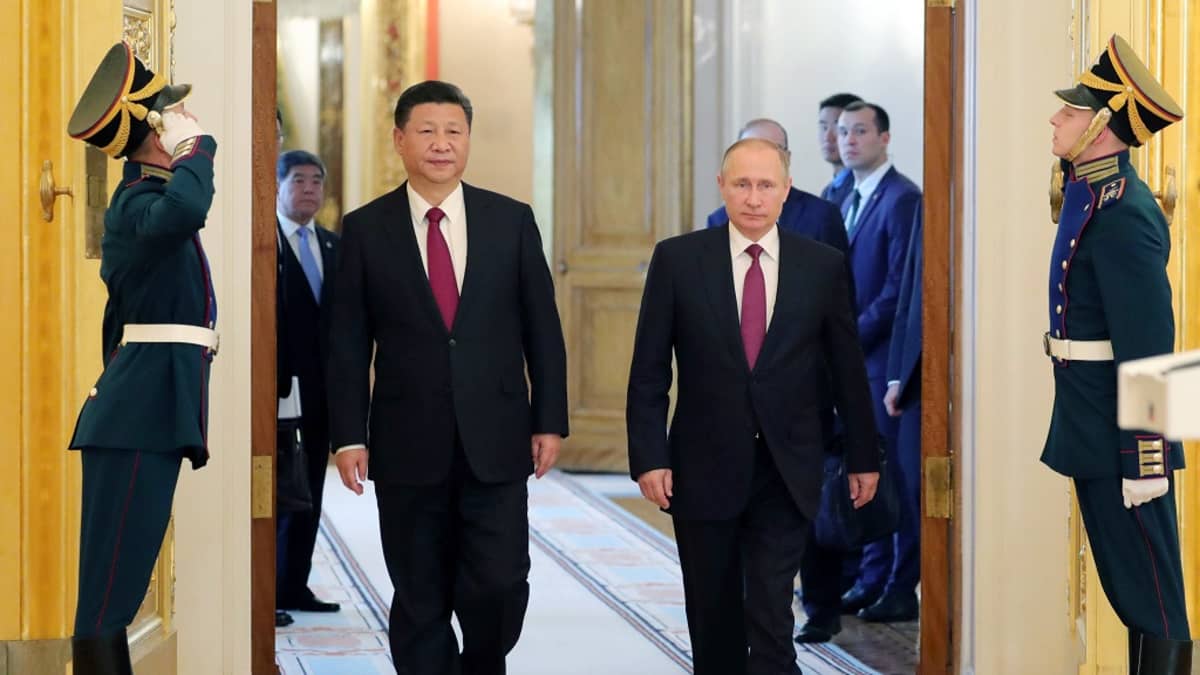 Xi ja Putin kävelevät saliin suuresta pariovesta. Miehillä on mustat puvut ja lähes identtisen punaiset kravatit. Oven molemmin puolin seisoo sotilas paraatiunivormussa ja tekee kunniaa tulijoille. Taustalla näkyy kiinalaisia ja venäläisiä virkamiehiä.
