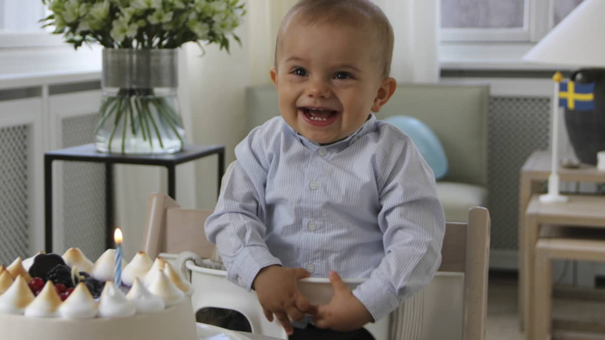 Oscar hymyilee syöttötuolissa, edessä kakku, jossa yksi kynttilä.